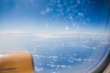 Bulutların üzerinde, bir uçağın kanadı gökyüzünde görünür, hava yolculuğu sırasında atmosferin engin genişliğini gösterir.