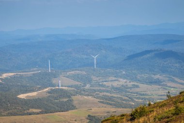 Göz kamaştırıcı bir hava manzarası, yemyeşil dağların arasına yerleşmiş sayısız rüzgar türbini sergiliyor.