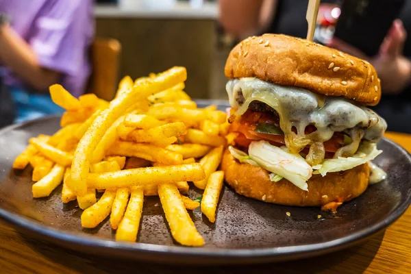 stock image Melted cheese oozing down a hot hamburger with seasoned french fries