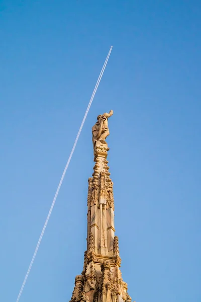 ミラノ大聖堂のスパイアとピンクの彫刻 バックグラウンドにクラウドトレイルの長い行を残す飛行機 — ストック写真