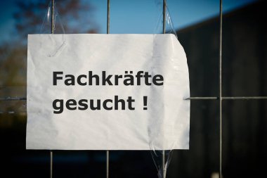  Notice on the fence of a company in Germany with the inscription Fachkrafte gesucht. Translation of the text: Professionals wanted                                 clipart