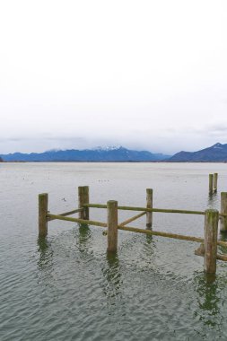 Remains of an old landing stage for boats in Prien am Chiemsee with the Chiemgau Alps in the background                                clipart
