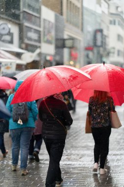  Almanya 'da Köln' de yağmurlu bir havada popüler bir alışveriş caddesinde kırmızı şemsiyeli insanlar                              