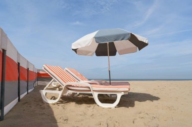  Batı Flanders, Belçika 'da De Haan yakınlarındaki Kuzey Denizi plajında güneşlik ve plaj sandalyesi.                              