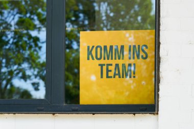 yellow sign with the German inscription komm ins Team, in an office window as a sign of the shortage of skilled workers. Translation: come into the team                                clipart
