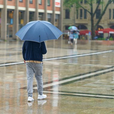  Almanya 'nın Köln şehir merkezinde yağmurda şemsiyeli genç bir adam.                              