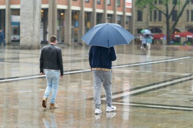 Köln, Almanya 24 Mayıs 2024: Almanya 'da Köln' de yağmur altında yaya bölgesinde iki genç adam                               