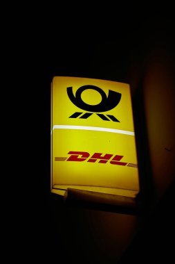  Berlin, Germany  March 30, 2024: Illuminated sign of a post office of the German logistics company DHL in Berlin in the evening                               clipart