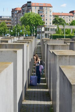  Berlin, Almanya 01 Mayıs 2025: Berlin şehir merkezindeki Yahudi Soykırımı Anıtı 'nın beton blokları arasında valizli kadın turist                              