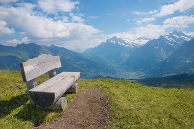wooden bench at Mannlichen mountain, view to Grindelwald tourist resort swiss alps. blue sky with clouds clipart