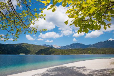 Eibsee Gölü kıyısı, yeşil yapraklı dalların arasından görünen, baharda yukarı bavyera