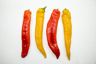 Dört uzun biber, kırmızı ve sarı, üst üste. Yumuşak bilyeli beyaz arkaplan