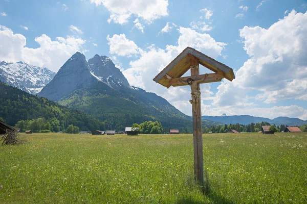 wayside cross at green pasture, view to Waxenstein mountains, spring landscape near Garmisch-Partenkirchen, upper bavarian tourist resort