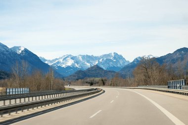 Kış mevsiminde Garmisch otoyolunda araba kullanmak. Yol kenarında çıplak ağaçlar.