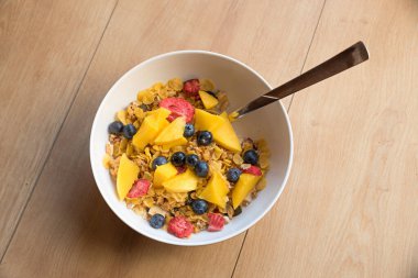 Yabanmersinli müsli, mangolu, çilekli ve mısır gevrekli. Porselen tabakta sağlıklı bir kahvaltı, ahşap arka plan. 