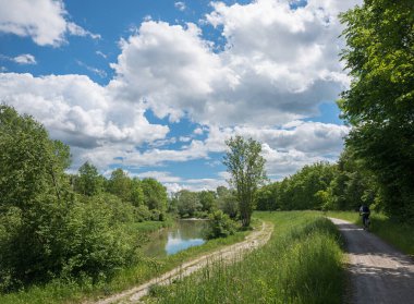 Mangfall nehri ve ağaçlı yeşil nehir kenarı, dağ manzaralı. Bulutlu mavi gökyüzü. Üst Bavyera manzarası. Motosikletli.. 