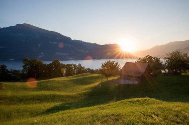 Thunersee Gölü üzerinde güzel bir gün batımı, Niederhorn Dağı manzarası, kulübe ile yeşil çayır, manzara değişikliği