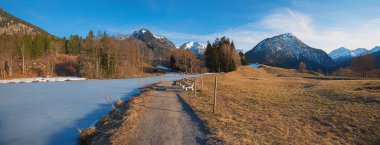 walkway along frozen lake Moorweiher, landscape near Oberstdorf, allgau alps in march. clipart