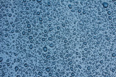 Bir sürü yağmur damlası olan mavi bir arabanın metalik yüzeyi, yakın çekim.