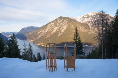 two wooden sledges at the  tobogganing run Pertisau, Tyrol with a view of Lake Achensee and Rofan alps. landscape at dawn with illuminated mountains. clipart