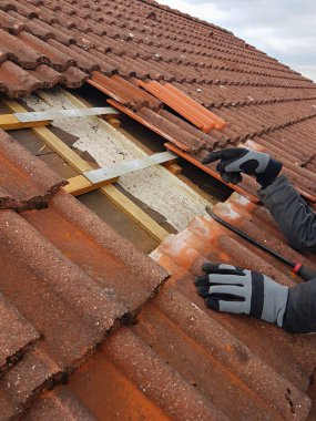 Adam çatıdaki kırık kiremitleri yenileriyle değiştiriyor. Yakın çekim, sadece kolları olan resim bölümü.