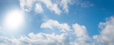 Solda güneşten gelen ışıkla mavi gökyüzü ve kabarık bulutlar, panorama