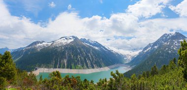 Dağ çam ağaçlarının üzerinden Schlegeisspeicher Gölü 'ne, Zillertal Alp Dağları yürüyüş merkezine, Mayrhofen yakınlarındaki Avustralya manzarasına. Bulutlu mavi gökyüzü.