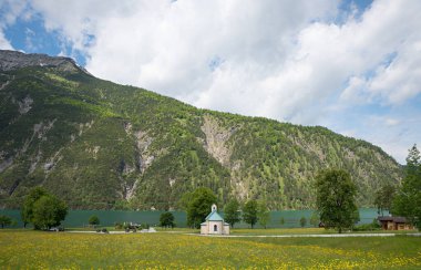 meadow with dandelions, small chapel at the lakeside of Achensee, landscape tyrol austria at springtime.
