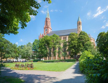 Münih Haidhausen, Johannisplatz 'ın park alanı tuğla kilise, çiçek yatakları ve yeşil ağaçlarla çevrili..