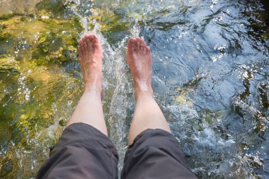 Yaşlı bir kadının ayakları ve bacakları soğuk bir nehrin suyunda ferahlatıcı.