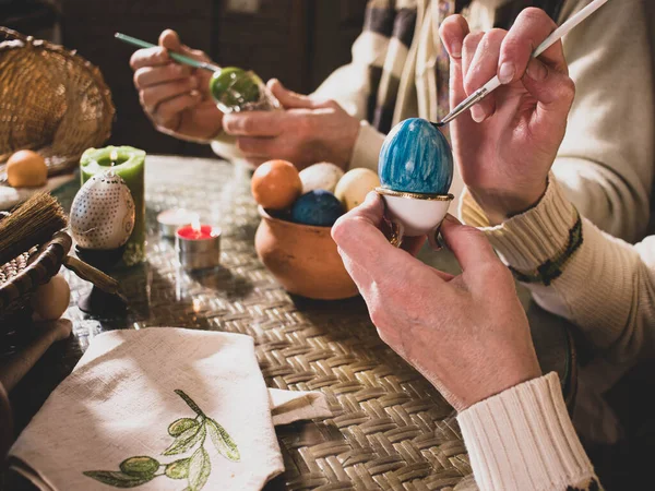 Yaşlı bir aile, bir erkek ve bir kadın tatil hazırlığı için bir fırçayla tavuk yumurtası boyarlar. Mutlu Paskalyalar