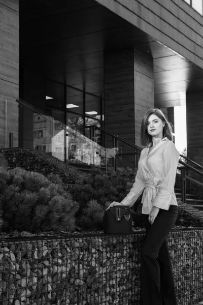 Bir iş binasının yanında şık giyinmiş güzel bir bayanın siyah beyaz fotoğrafı.