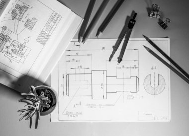 Mühendis ya da tasarımcının masası. Masanın üzerinde teknik diyagramları ve detayları olan çizimler var, çizim araçları yakında. Çizimlerin yanında bir saksı görülebilir, bu da çalışma alanına rahatlık katar..