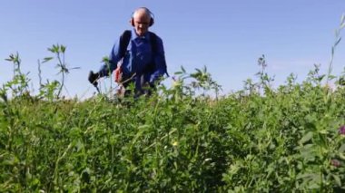 Tulumlu adam hayvanlar için uzun otlar biçiyor. Bahçe işleri, bakım, açık hava işleri ve mevsimlik bahçe bakımı kavramı.