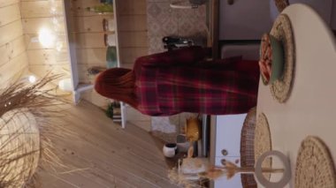 Genç kızıl saçlı bir kadın, ahşap bir evin rahat mutfağında bir şişe şarap ve bir bardakla. Dikey video