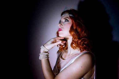 Kızıl saçlı, 1920 'lerin modasını andıran şık beyaz elbiseli genç bir kadın. Tüylü parlak bir saç bandıyla görünüşü tamamlanmış. Zarafet ve klasik bir cazibe katıyor.. 