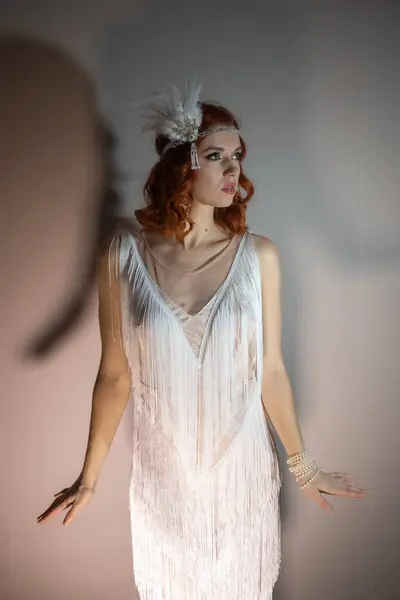 1920 'lerden kalma püsküllü bir elbise giymiş güzel bir kadının fotoğrafı. Kızıl saçları var, tüy şeklinde bir aksesuarla süslenmiş..