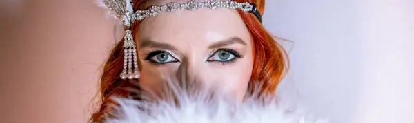 Makyajlı bir kızın portresi, yüzü kuş tüyü bir yelpaze ile kaplı. Gözler pankartta.