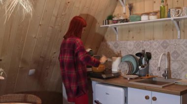 Kareli gömlekli kızıl saçlı bir kadın sevgilisi için akşam yemeği hazırlar. Romantizm atmosferi, sıcaklık ve ev konforu..