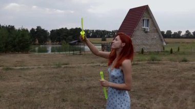 Kızıl saçlı bir kadın baloncuklarla oynar doğal bir arka plan ile rahat bir evi, göleti ve ormanı olan.