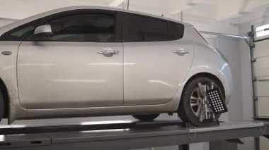 Tekerlek geometrisini kontrol etmek için tribün kullanan bir elektrikli aracın tekerlek hizalanmasının teşhisi. Tekerleklere bir ölçüm cihazı bağlanmış.,