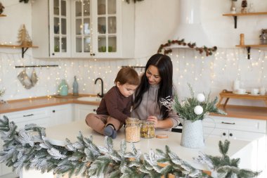 Anne ve oğlu Noel süslemeli mutfakta oynuyor ve eğleniyorlar. Mutlu aile tatili bekliyor.