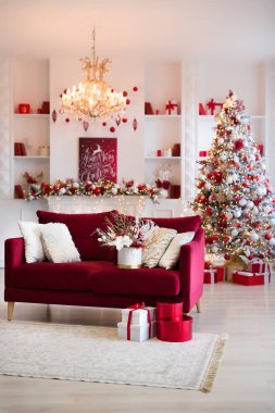 İçinde şömine, avize ve Noel ağacı ve kırmızı hediyelerle süslenmiş rahat bir kanepe olan parlak, modern bir oturma odası. Dikey fotoğraf