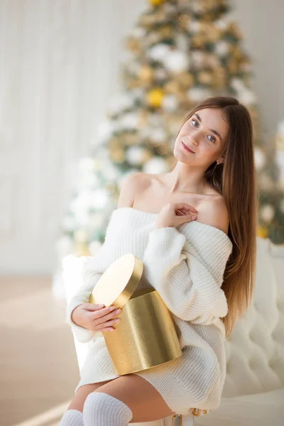 クリスマスを祝う幸せな若い美しい女性 白いセーターの女の子はクリスマスツリーの背景に贈り物を保持します クリスマスのコンセプト ギフトボックスと笑顔の女性 — ストック写真