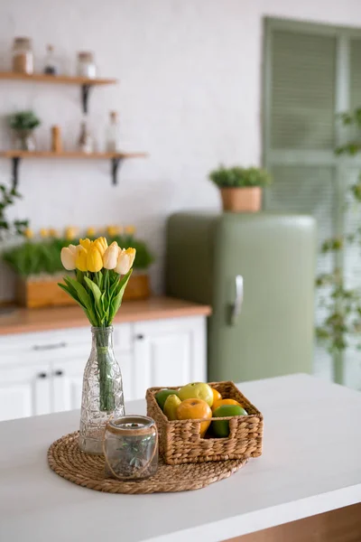 A bouquet of tulips on a white table. In the background, the interior of a white kitchen in the Scandinavian style. The concept of home comfort