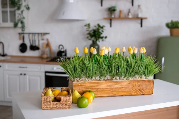 A bouquet of tulips on a white table. In the background, the interior of a white kitchen in the Scandinavian style. The concept of home comfort
