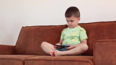 Küçük çocuk, parmaklarını telefon ekranına bastırıp kaydırıyor. Şirin küçük çocuk yeni internet teknolojileri kullanmayı öğreniyor. Bebek evde cep telefonuyla oynuyor..