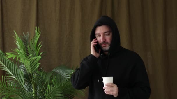 Λευκός Άντρας Μαύρη Κουκούλα Πίνει Καφέ Και Μιλάει Στο Τηλέφωνο — Αρχείο Βίντεο