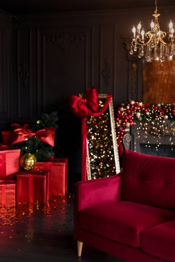 Lüks karanlık oturma odasının içinde şöminesi, rahat koltuğu ve Noel ağacıyla süslenmiş avizesi ve kırmızı renkli hediyeleri var..