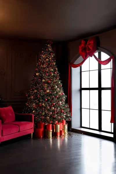 Interior of luxury dark living room with fireplace, comfortable sofa and chandelier decorated with Christmas tree and gifts in red color.